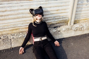 Young diverse no make up woman outdoor lying floor using augmented reality headset cyber dependent