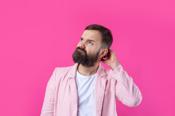 Handsome man with a beard in a pink jacket is thinking over an isolated red background.