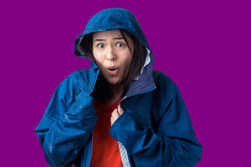 Portrait of a smiling girl dressed in blue raincoat in drops posing with hood on grey background in a studio.