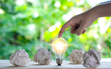 great idea concept with crumpled office paper and light bulb standing on table with green nature background. Saving world ecology. 