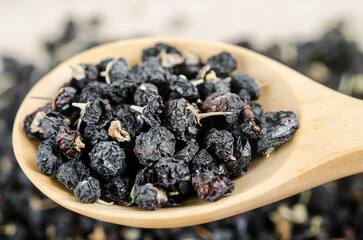 Black wolfberries or black goji berries, in a wooden spoon on table.