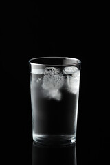 Cold water and ice cubes in glass on black background