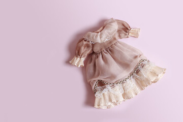Beautiful vintage dress with ruffles for a doll on a pink background with copy space