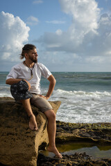 Attractive Caucasian man sitting on a stone at the beach.