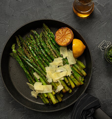 Fried green asparagus with lemon and parmesan in a pan.  Black marble table with olive oil and pesto. Top view.