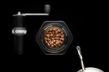 Brewing coffee alternative method. Aeropress with coffee beans and kettle in focus, coffee grinder blurred. Black background top view.