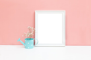 Mockup of a white wooden frame with a watering can and a white flower on the table