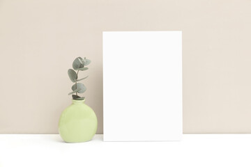 Wedding invitation or greeting card mockup with a vase and a sprig of eucalyptus on a beige...