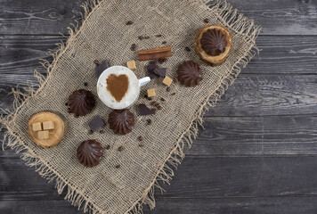 coffee with milk with marshmallows in chocolate and cane sugar on burlap on dark wooden background in rustic style, flat lay with copy space