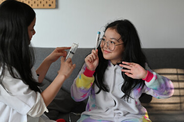 A portrait of a cute Asian girl wearing a doctor coat playing roles as a doctor and patient, holding a thermometer, for education, career, health and family concept.