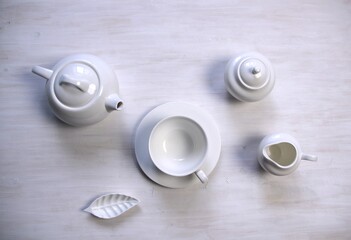 white still life with  tea cup and saucer, teapot, milk jug, creamer, sugar bowl  on  wooden table