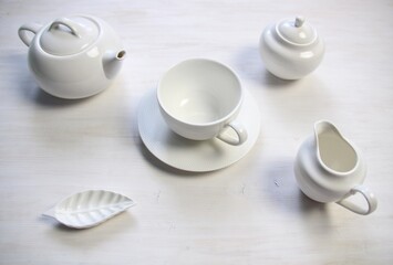 Fototapeta na wymiar white tea cup and saucer, teapot, milk jug, creamer, sugar bowl on white wooden table