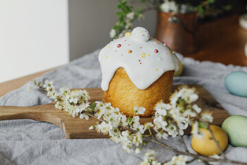 Happy Easter!  Homemade easter bread, natural dyed eggs and spring blossom on rustic table in room. Stylish freshly baked easter cake with sugar glaze and sprinkles, traditional ukrainian bun