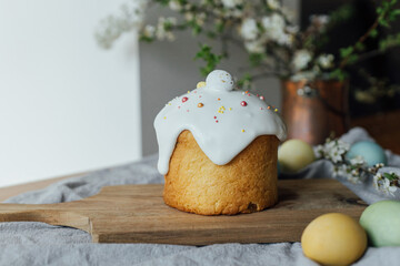 Happy Easter!  Homemade easter bread, natural dyed eggs and spring blossom on rustic table in room. Stylish freshly baked easter cake with sugar glaze and sprinkles, traditional ukrainian bun