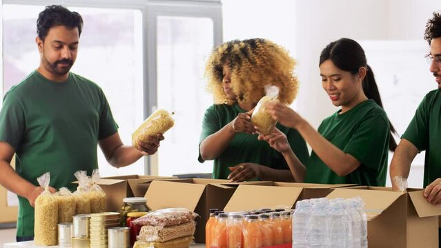 charity, donation and volunteering concept - international group of happy smiling volunteers packing food in boxes at distribution or refugee assistance center