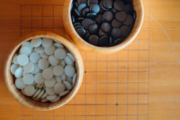 Obraz na płótnie Canvas A set of Go or Igo game stones in the wooden bowls on the grid table.
