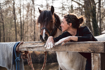 Smiling woman horse owner talks with her pony and showing hands full with animal hair in spring shedding season