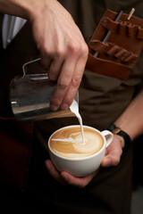 Barista hands pouring milk in coffee cup, close-up