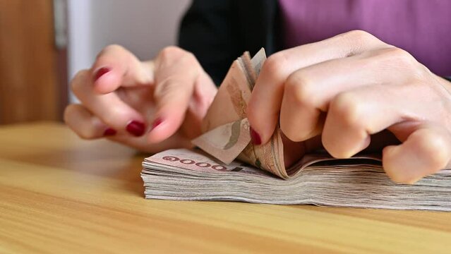 Close up of woman with red fingernails counting Thai baht banknotes. The baht is the official currency of Thailand.
