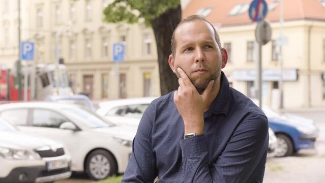 A Caucasian man thinks about something in an urban area - a colorful street in the blurry background