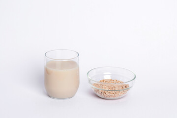 A glass of non dairy oat milk and oat flakes on white table. Healthy food concept