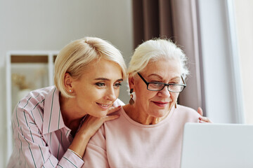 Close up portrait of young woman with senior mother using computer together at home and shopping...