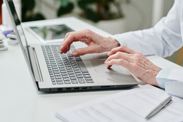 Hands of contemporary experienced online doctor over laptop keyboard during online consultation of patients and answering their questions