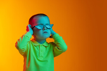Portrait of cute little boy smiling isolated on yellow studio backgroud in neon light. Concept of child emotions, facial expression, childhood