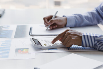 Businessman works on analyzing financial data using a calculator and writing notes with...