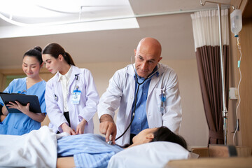 Group of doctor visiting ward have woman patient and check her with stethoscope on bed. Woman patient lying on hospital bed while doctor giving her checkup.