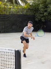 Young adult bearded man wearing cap plays tennis outdoors.