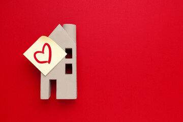Miniature of a house with a heart on a red background, empty space for text.