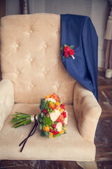 The bride's bouquet and the groom's jacket with a boutonniere on an antique upholstered armchair in the bedroom