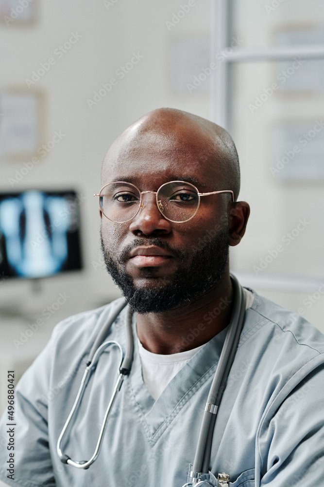 Poster young confident black man in uniform and eyeglasses looking at camera while sitting by workplace aga