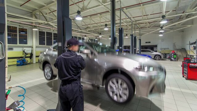 Car mechanic screwing and unscrewing car wheel of lifted automobile at repair service station timelapse hyperlapse