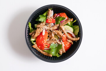 Vegetable salad with tomatoes and meat and sesame in a disposable bowl.