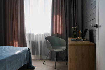 Part of comfortable bedroom with workplace of freelancer in the corner by window with white chiffon...