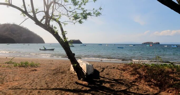 Tropical sandy beach with a tree, small waves on a sunny day, Coco Beach in Guanacaste, Costa Rica.  View of Pacific Ocean with small islands and wooden  boats
