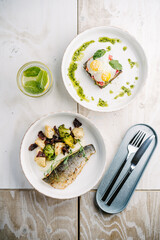 Sea bass with creamy lemon sauce and vegetables with Smorrebrod, Danish open sandwich with salmon, egg, avocado and cilantro sauce