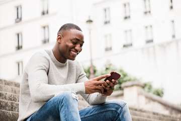 smiling African american man sitting outside in city using cellphone