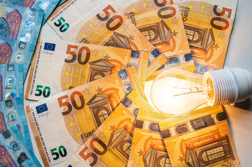 Light bulb turned on, with Euro banknotes around. Increase in electricity tariffs, energy...