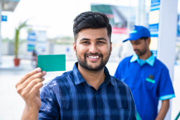 Smiling customers showing green empty card by looking camera at petrol pump - concept of employee...