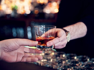 Hands of a pub customer and bartender serving a glass of neat whiskey. Close up view.
