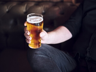 Hipster man sitting at the pub or bar couch and drinking a glass of beer.