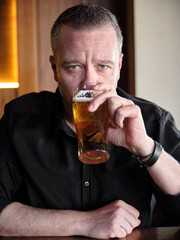 Portrait of a hipster man in his 40s drinking a glass of beer in a bar or pub.