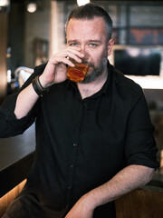 Portrait of a handsome mature man drinking a glass of neat whiskey at the bar or pub.