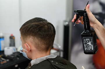 A teenager in a beauty salon gets a haircut, a hairdresser cuts a teenage boy's hair.