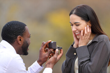 Interracial couple proposing marriage in a park - obrazy, fototapety, plakaty