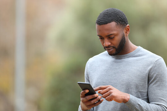 Man with black skin using cell phone walking in a park