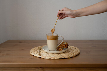 Dalgona coffee in a glass on a wooden table. Hand with a long spoon.